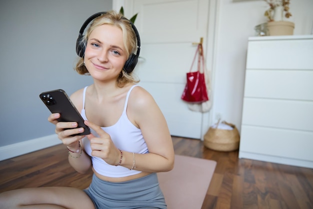 Ritratto di una donna in fitness sorridente che indossa cuffie wireless con un telefono cellulare che si allena con