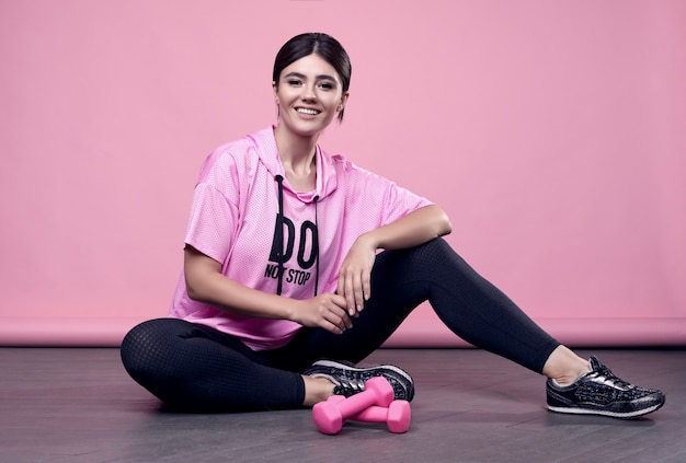 Ritratto di una donna latina positiva del corpo splendido in una felpa con cappuccio rosa di sport che si esercita con le teste di legno sul rosa