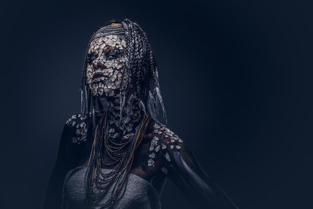 Ritratto di una donna sciamana africana spaventosa con una pelle screpolata pietrificata e dreadlocks su uno sfondo scuro. Concetto di trucco.