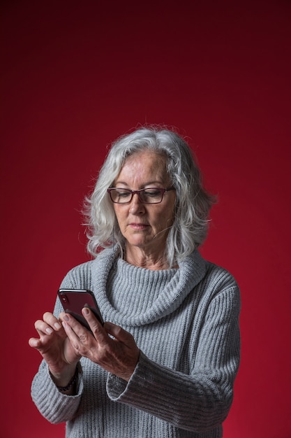 Ritratto di una donna senior che utilizza smartphone contro il contesto rosso