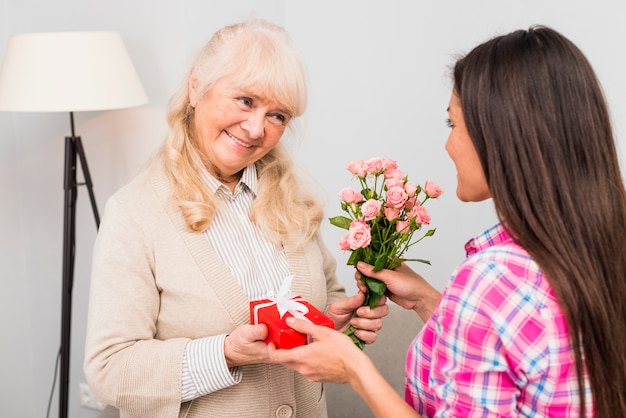 Ritratto di una donna senior sorridente che dà regalo e rose alla sua giovane figlia