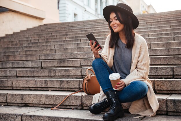 Ritratto di una donna sorridente attraente che per mezzo del telefono cellulare