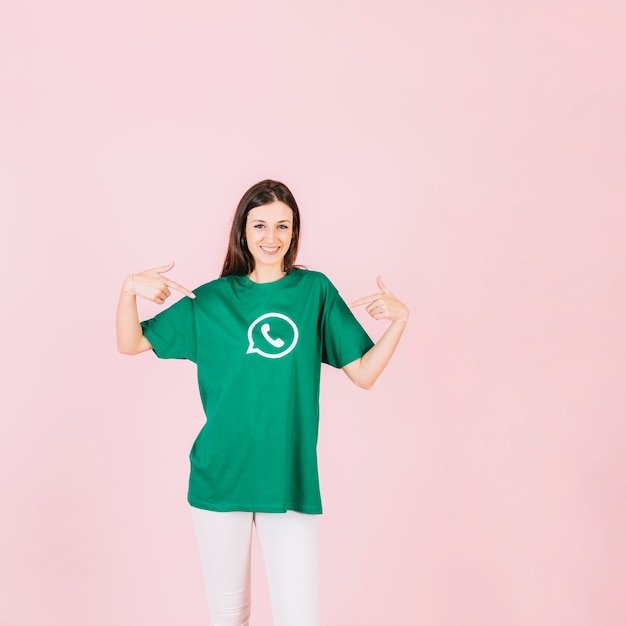 Ritratto di una donna sorridente che punta alla sua t-shirt con l&#39;icona di WhatsApp