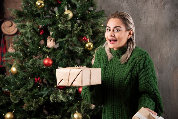 Ritratto di una donna vestita in maglione verde che tiene pila di scatole regalo e che guarda l'obbiettivo