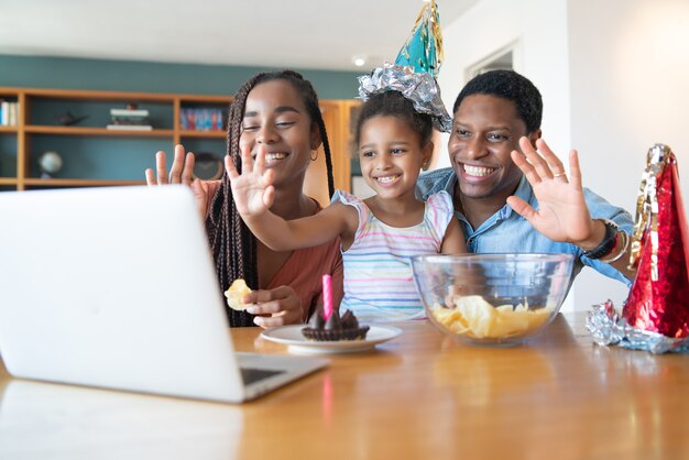 Ritratto di una famiglia che festeggia il compleanno online durante una videochiamata con un laptop restando a casa. Nuovo concetto di stile di vita normale.