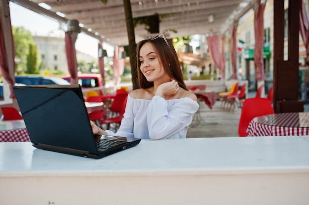 Ritratto di una forte donna d'affari di successo indipendente che indossa abiti casual intelligenti e occhiali che lavorano su un laptop in un caffè