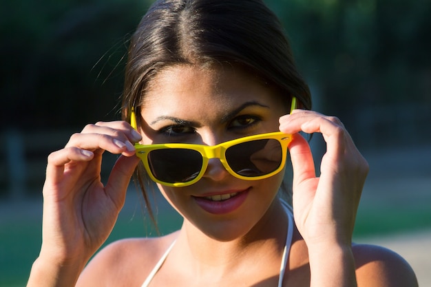 Ritratto di una giovane bella donna in un parco con occhiali da sole gialli