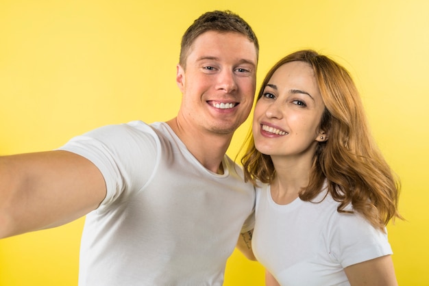 Ritratto di una giovane coppia sorridente prendendo selfie contro sfondo giallo