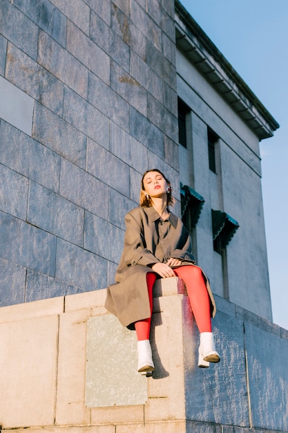 Ritratto di una giovane donna alla moda che si siede oltre il muro