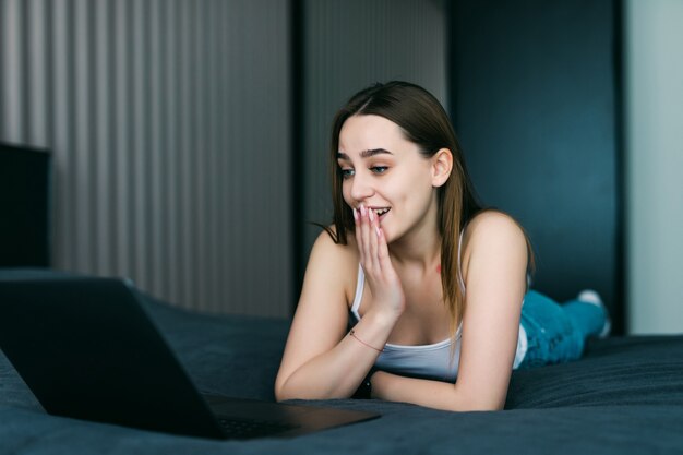 Ritratto di una giovane donna casuale scioccata utilizzando laptop a letto