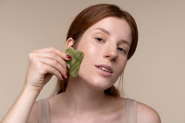 Ritratto di una giovane donna che si massaggia il viso usando un gua sha