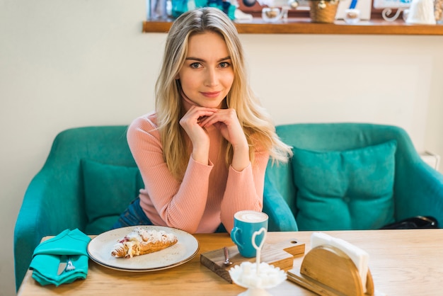 Ritratto di una giovane donna che si siede al tavolo con croissant e tazza di caffè
