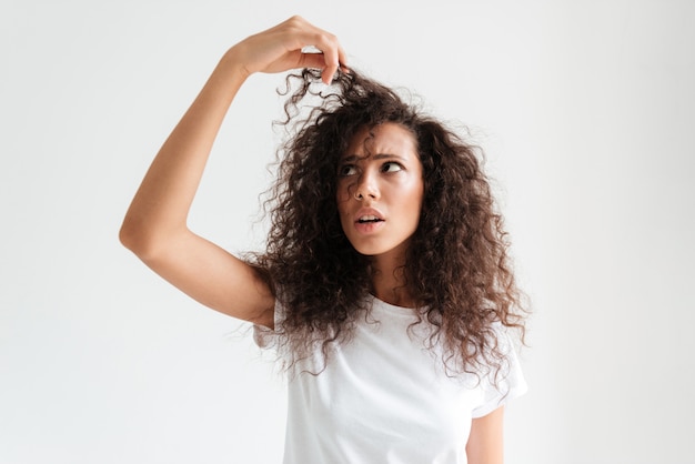 Ritratto di una giovane donna confusa guardando i suoi capelli