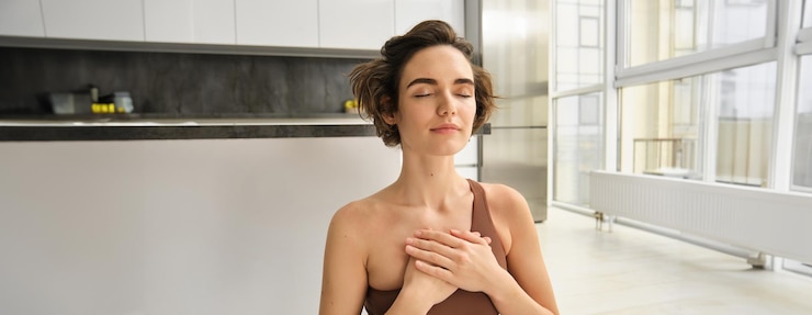 Foto gratuito ritratto di una giovane donna consapevole che apre il suo chakra facendo yoga su un tappetino di gomma a casa chiude gli occhi e
