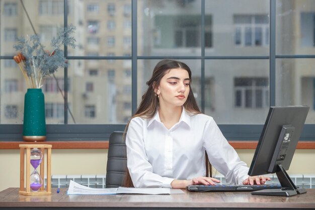 Ritratto di una giovane donna di affari che si siede alla scrivania e che lavora al pc