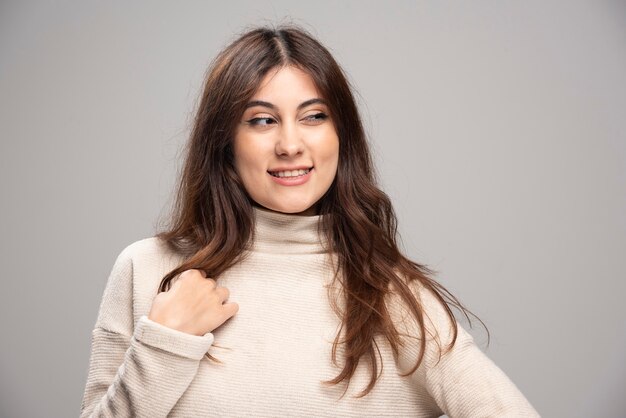 Ritratto di una giovane donna in posa su un muro grigio.