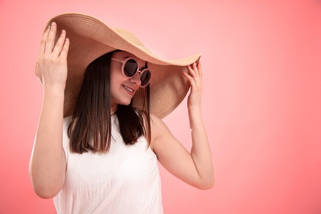 Ritratto di una giovane donna in un grande cappello estivo e occhiali in rosa