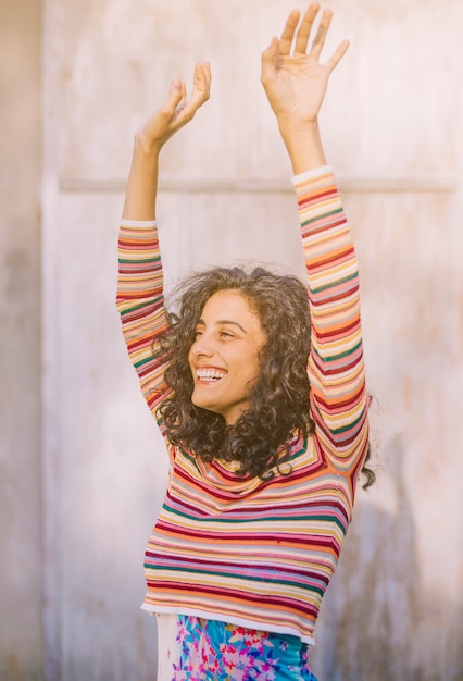 Ritratto di una giovane donna sorridente che alza le sue braccia contro il muro