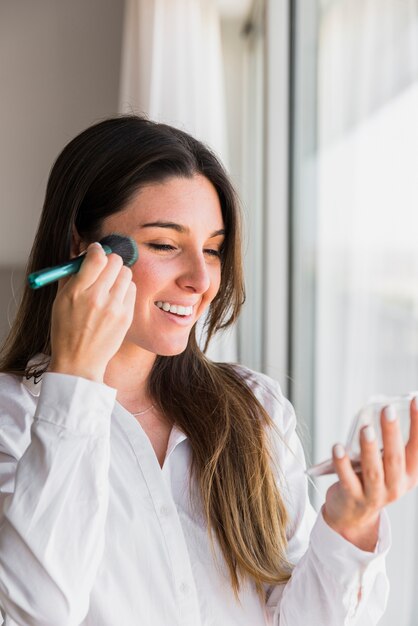 Ritratto di una giovane donna sorridente che applica la cipria con la spazzola di trucco