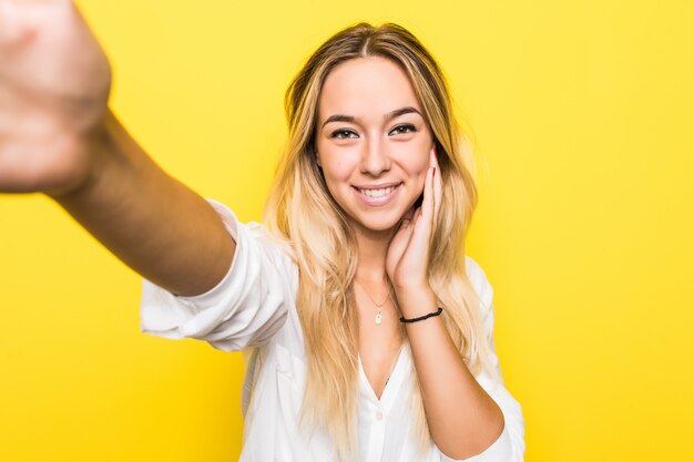Ritratto di una giovane donna sorridente che cattura un selfie sopra la parete gialla