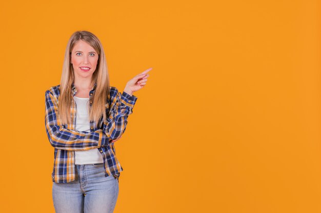 Ritratto di una giovane donna sorridente che punta il dito contro uno sfondo arancione