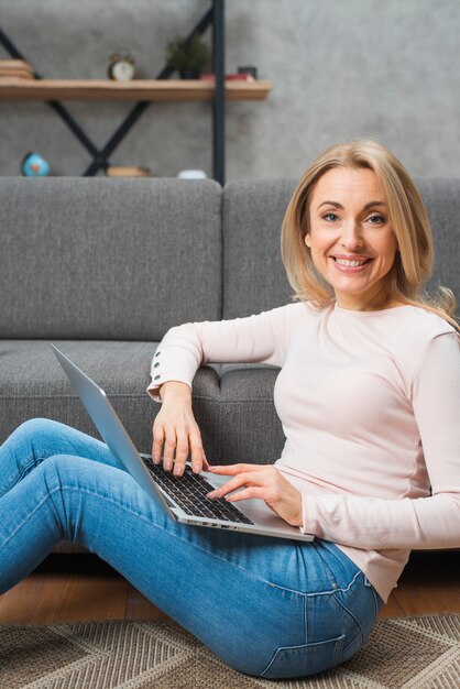 Ritratto di una giovane donna sorridente che si siede sul tappeto con laptop