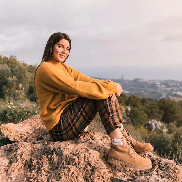 Ritratto di una giovane donna sorridente che si siede sulla cima della montagna che guarda l&#39;obbiettivo