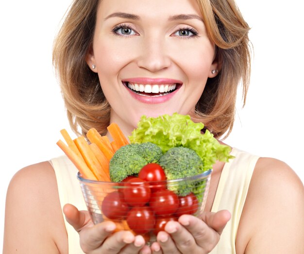 Ritratto di una giovane donna sorridente con un piatto di verdure isolato su bianco.