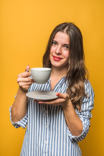 Ritratto di una giovane donna sorridente tenendo piattino e tazza nelle mani