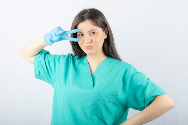 Ritratto di una giovane dottoressa in uniforme verde che mostra il segno della vittoria.