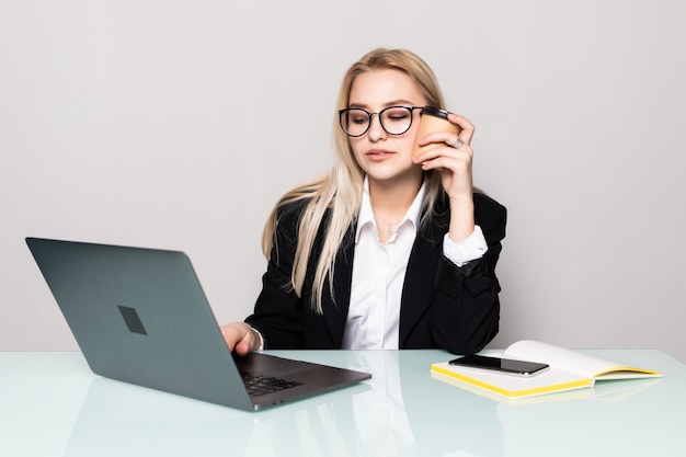 Ritratto di una giovane e attraente donna d'affari seduto alla sua scrivania con una conversazione telefonica e utilizzando un computer portatile, isolato su un muro bianco.