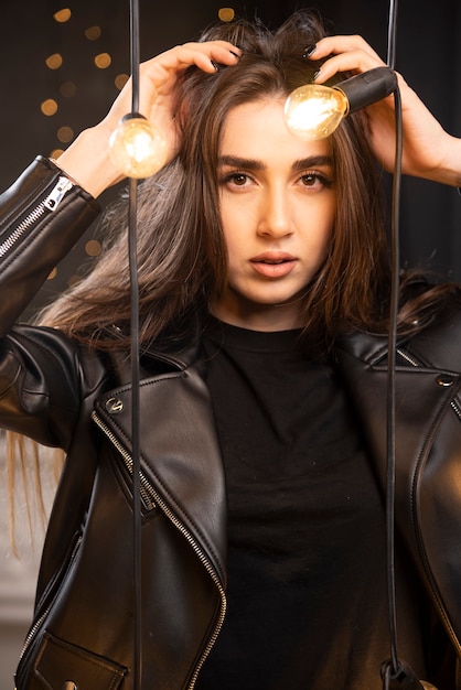 Ritratto di una giovane modella in giacca di pelle nera in posa vicino a lampade.
