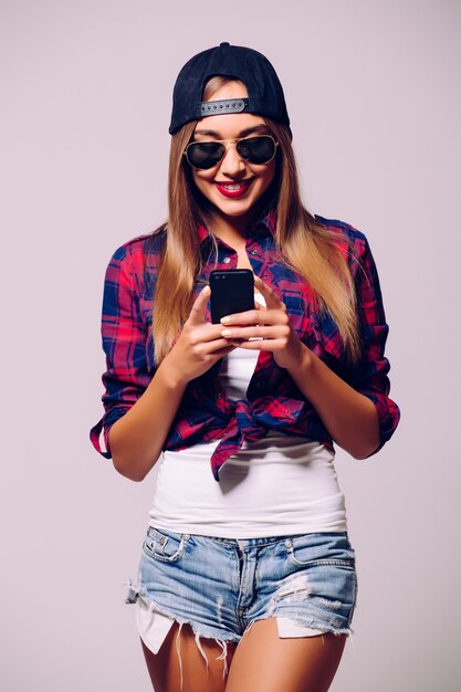 Ritratto di una giovane ragazza felice utilizza lo smartphone isolato su un muro grigio