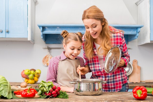 Ritratto di una madre e una figlia sorridenti che esaminano alimento preparato sulla tavola di legno