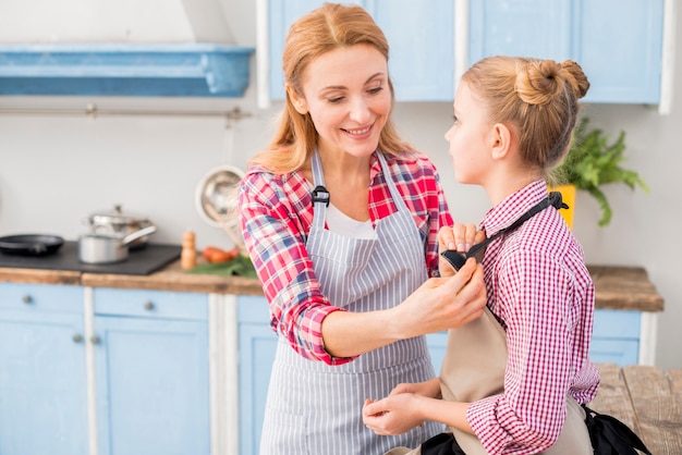 Ritratto di una madre sorridente che mette la cinghia di grembiule in cucina