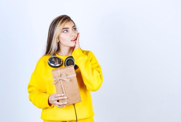 Ritratto di una modella che tiene in mano una scatola di carta con fiocco isolato su un muro bianco