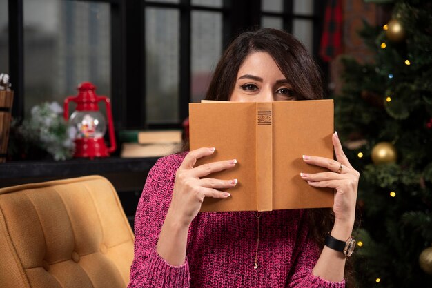 Ritratto di una ragazza abbastanza giovane che si nasconde dietro un libro aperto.