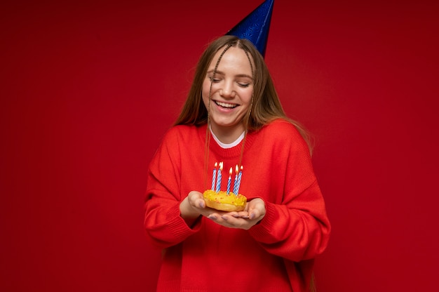 Ritratto di una ragazza adolescente che indossa un cappello da compleanno e tiene in mano una ciambella con candele di compleanno