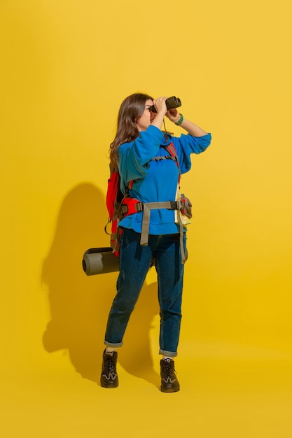 Ritratto di una ragazza allegra giovane turista con borsa e binocolo isolato sulla parete gialla dello studio