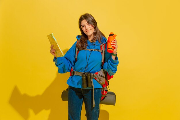 Ritratto di una ragazza allegra giovane turista con borsa e binocolo isolato sulla parete gialla dello studio