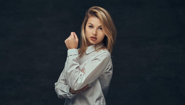 Ritratto di una ragazza bionda sensuale vestita con una camicia bianca, in posa in uno studio. Isolato su uno sfondo scuro.