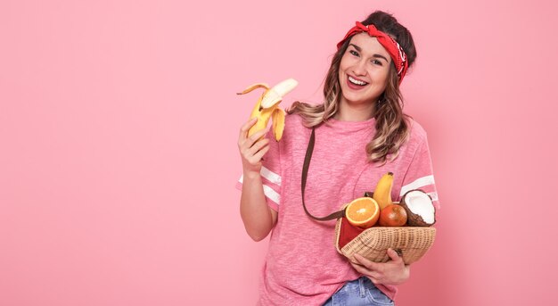 Ritratto di una ragazza con cibo sano, frutta, su una parete rosa