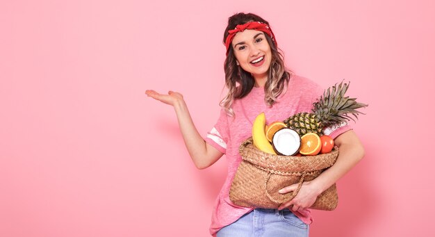 Ritratto di una ragazza con una borsa con frutta isolata su una parete rosa