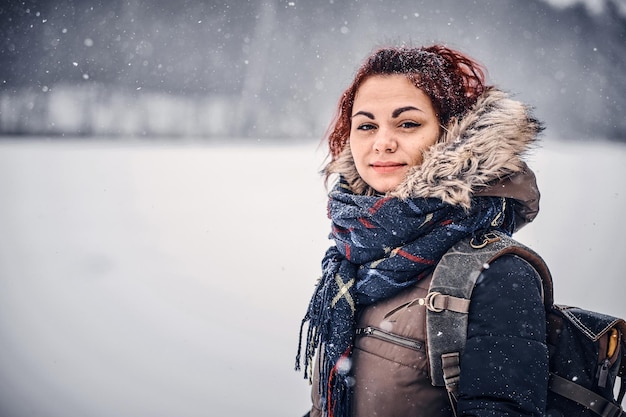 Ritratto di una ragazza dai capelli rossi con uno zaino che cammina attraverso la foresta invernale