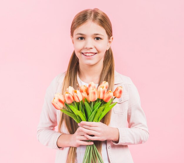 Ritratto di una ragazza felice che guarda alla macchina fotografica che giudica il mazzo dei tulipani a disposizione che sta contro il fondo rosa