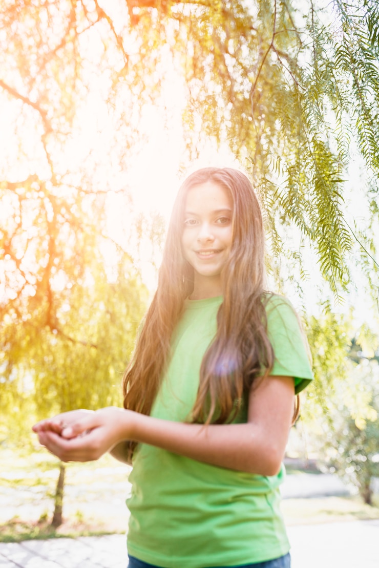 Foto gratuito ritratto di una ragazza felice in piedi sotto l'albero al sole