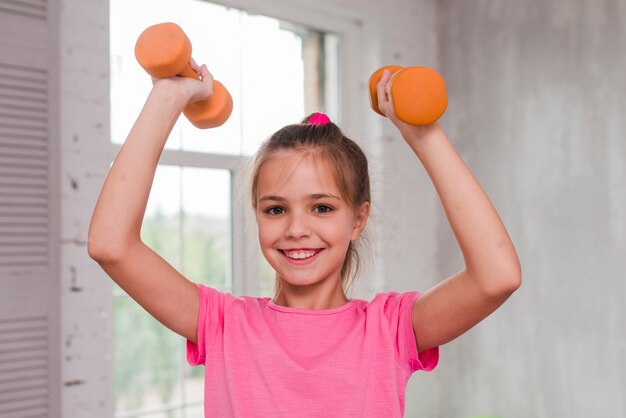 Ritratto di una ragazza sorridente che si esercita con un dumbbell arancione