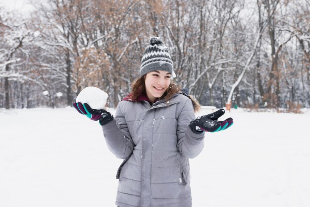 Ritratto di una ragazza sorridente graziosa che tiene palla di neve alla foresta