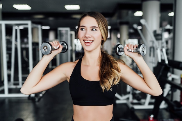 Ritratto di una ragazza sportiva attraente con manubri in mano, tempo per lo sport, allenamento, palestra moderna.