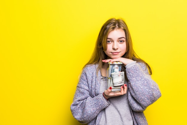 Ritratto di una ragazza teenager del brunette con i soldi del cuppingglass isolati. Pentola con soldi nelle mani degli adolescenti